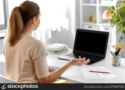 distant education, remote job and people concept - happy smiling female teacher with laptop computer having video call or online class at home office. treacher with laptop having video call at home