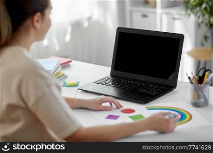distant education, school and people concept - female elementary school teacher with laptop computer and picture of geometric shapes in different colors having online class at home. teacher having online class at home