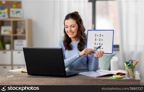 distant education, school and people concept - happy smiling female math teacher with laptop computer and mathematics having online class at home. math teacher having online class at home