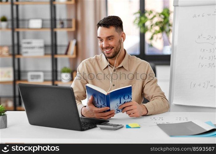 distant education, school and remote job concept - happy smiling male math teacher with laptop computer, book and flip chart having online class or video call at home office. math teacher with laptop and book at home office