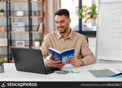 distant education, school and remote job concept - happy smiling male math teacher with laptop computer, book and flip chart having online class or video call at home office. math teacher with laptop and book at home office
