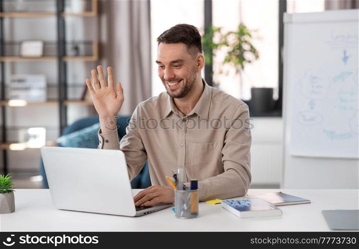 distant education, school and remote job concept - happy smiling male teacher with laptop computer having online class at home office and waving hand. teacher with laptop having online class at home
