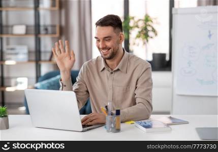 distant education, school and remote job concept - happy smiling male teacher with laptop computer having online class at home office and waving hand. teacher with laptop having online class at home