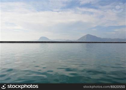 Distant hills sea and cloudy sky horizon landscape. Seawall pier on port of Patras, Greece.