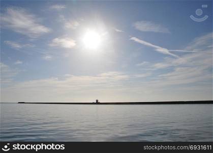 Distant pier breakwater wall blue sea and sunny sky horizon abstract landscape.