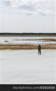 Distant view of a man standing by a lake with a reed among white sandy desert. Quarry for the development of quartz sand, Moscow region, Russia. Selective focus, desaturated colors.