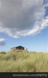 Distant View Of Young Couple Relaxing In Wooden Beach Hut Amongst Dunes
