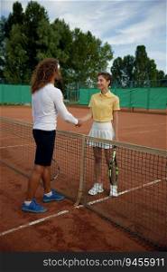 Diverse tennis players shaking hands after successful training on court outdoors. Cheerful young man and woman in sports uniform celebrating sport game competition finish. Diverse tennis players shaking hands after successful training on court