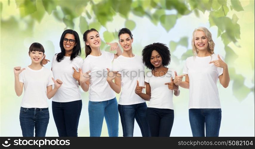 diversity, ecology and people concept - international group of happy smiling volunteer women pointing to white blank t-shirts over green natural background. international volunteer women in white t-shirts