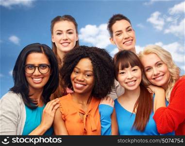 diversity, ethnicity and people concept - international group of happy smiling different women hugging over blue sky and clouds background. international group of happy women hugging