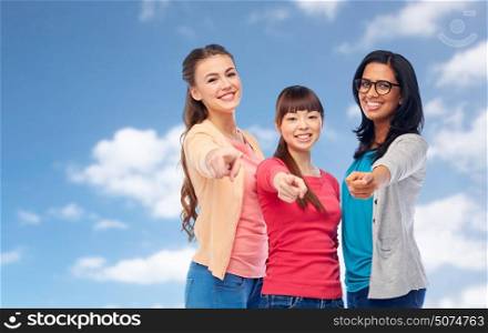 diversity, ethnicity and people concept - international group of happy smiling different women pointing finger at you over blue sky and clouds background. international happy women pointing finger at you