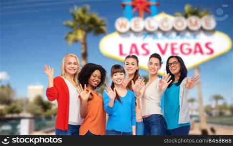 diversity, ethnicity, tourism and travel concept - international group of happy smiling different women or friends waving hands over welcome to fabulous las vegas sign background. international group of happy women at las vegas