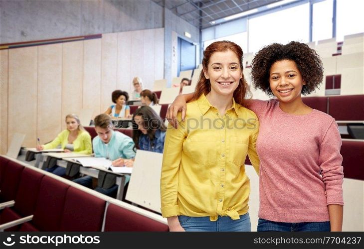 diversity, friendship and education concept - happy smiling student women hugging over university background. happy smiling student women hugging at university