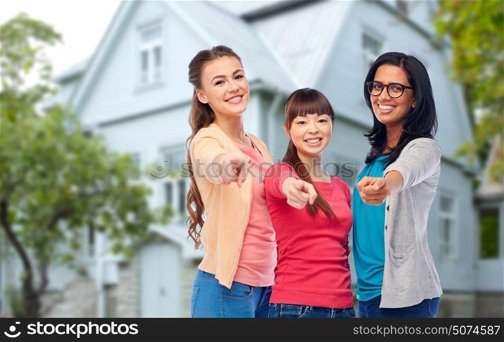 diversity, friendship and people concept - international group of happy smiling different women pointing finger at you over house background. international happy women pointing finger at you