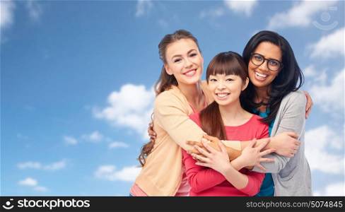 diversity, friendship and people concept - international group of happy smiling different women hugging over blue sky and clouds background. international group of happy women hugging