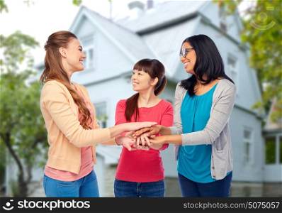diversity, friendship and people concept - international group of happy smiling different women holding hands together over house background. international group of women with hands together
