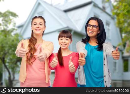 diversity, friendship and people concept - international group of happy smiling different women showing thumbs up over house background. international happy women showing thumbs up