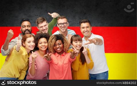 diversity, immigration and people concept - international group of happy smiling men and women showing thumbs up and peace over german flag background