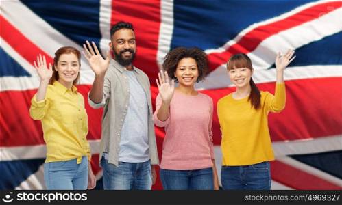 diversity, immigration and people concept - international group of happy smiling men and women waving hands over british flag background. international group of happy people waving hands