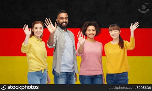 diversity, immigration and people concept - international group of happy smiling men and women waving hands over german flag background. international group of happy people waving hands