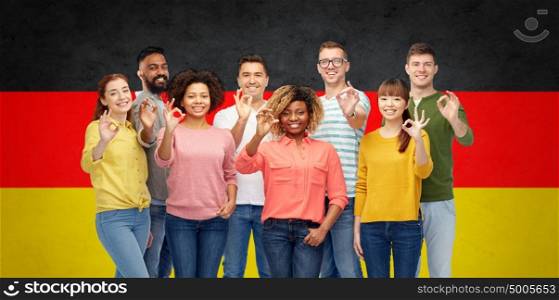 diversity, immigration, race, ethnicity and people concept - international group of happy smiling men and women showing ok hand sign over german flag background. international people showing ok over german flag