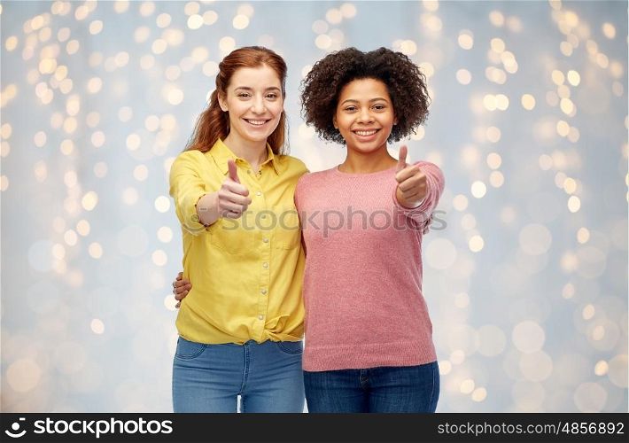 diversity, international, ethnicity, friendship and people concept - happy smiling women showing thumbs up and hugging over holidays lights background
