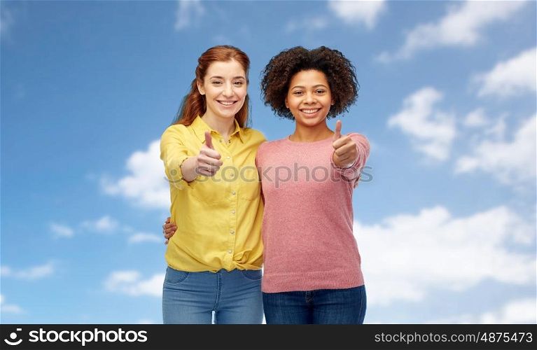 diversity, international, ethnicity, friendship and people concept - happy smiling women showing thumbs up and hugging over blue sky and clouds background