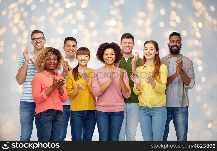 diversity, race, ethnicity and people concept - international group of happy smiling men and women applauding over holidays lights background