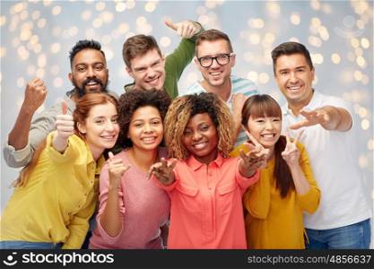 diversity, race, ethnicity and people concept - international group of happy smiling men and women showing thumbs up and peace over holidays lights background