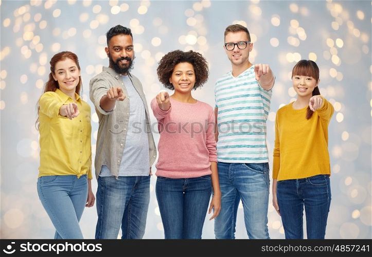 diversity, race, ethnicity and people concept - international group of happy smiling men and women pointing finger on you over holidays lights background