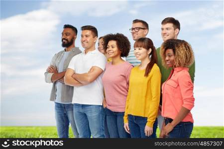 diversity, race, ethnicity and people concept - international group of happy smiling men and women over blue sky and grass background