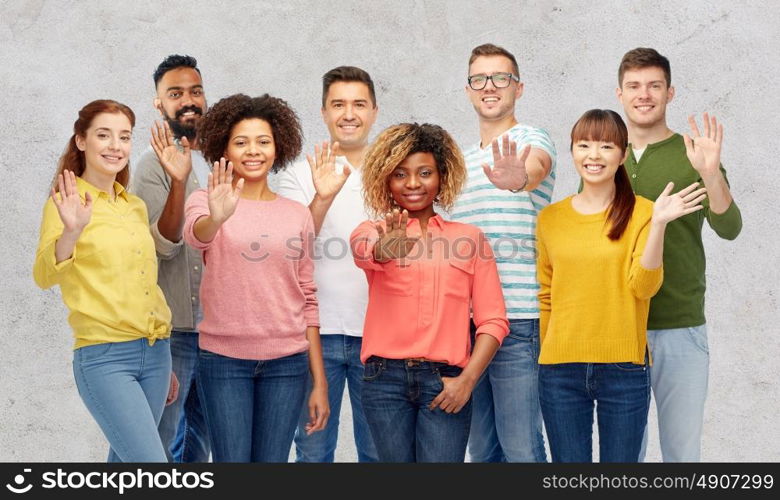 diversity, race, ethnicity and people concept - international group of happy smiling men and women waving hand over gray concrete background. international group of happy people waving hand