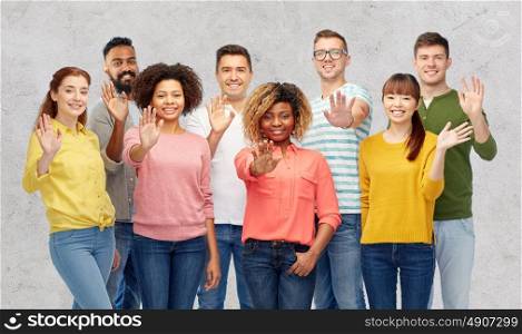 diversity, race, ethnicity and people concept - international group of happy smiling men and women waving hand over gray concrete background. international group of happy people waving hand
