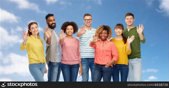 diversity, race, ethnicity and people concept - international group of happy smiling men and women waving hand over blue sky and clouds background. international group of happy people waving hand