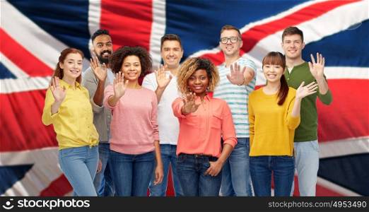 diversity, race, ethnicity and people concept - international group of happy smiling men and women waving hand over english flag background. international group of happy people waving hand