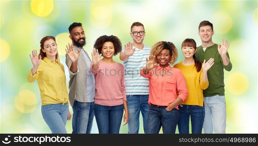 diversity, race, ethnicity and people concept - international group of happy smiling men and women waving hand over green holidays lights background. international group of happy people waving hand