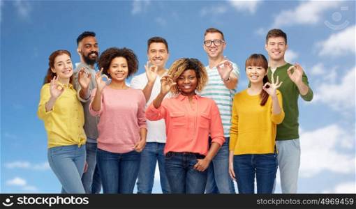 diversity, race, ethnicity and people concept - international group of happy smiling men and women showing ok hand sign over blue sky and clouds background. international group of happy people showing ok