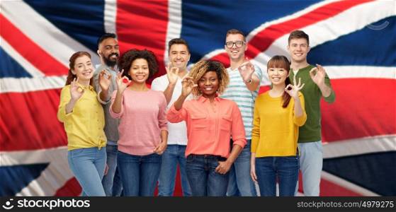 diversity, race, ethnicity and people concept - international group of happy smiling men and women showing ok hand sign over british or english flag background. international people showing ok over british flag