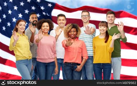 diversity, race, ethnicity and people concept - international group of happy smiling men and women waving hand over american flag background. international group of happy people waving hand