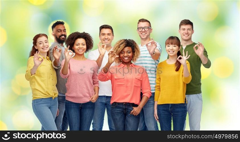 diversity, race, ethnicity and people concept - international group of happy smiling men and women showing ok hand sign over green holidays lights background. international group of happy people showing ok