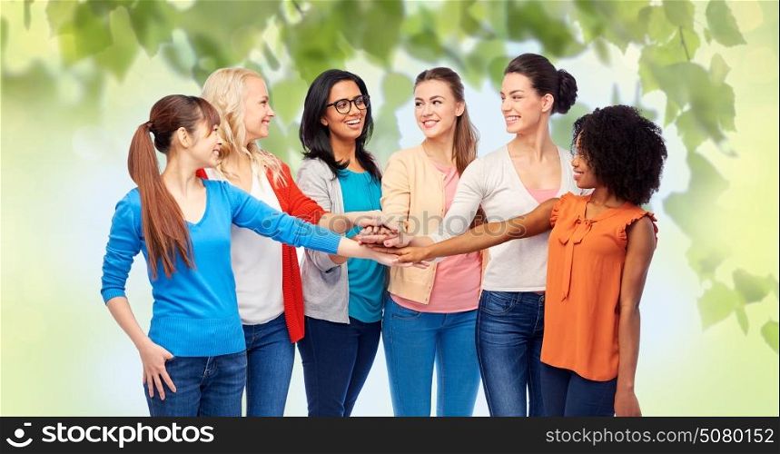 diversity, race, ethnicity and people concept - international group of happy smiling different women holding hands together over green natural background. international group of women with hands together