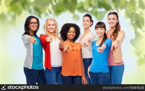 diversity, race, ethnicity and people concept - international group of happy smiling different women pointing finger at you over green natural background. international group of happy smiling women