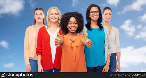 diversity, race, ethnicity and people concept - international group of happy smiling different women over white showing thumbs up over blue sky and clouds background. international group of women showing thumbs up