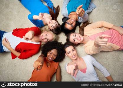 diversity, race, ethnicity and people concept - international group of happy smiling different women lying on floor in circle and pointing finger at you. international group of happy smiling women