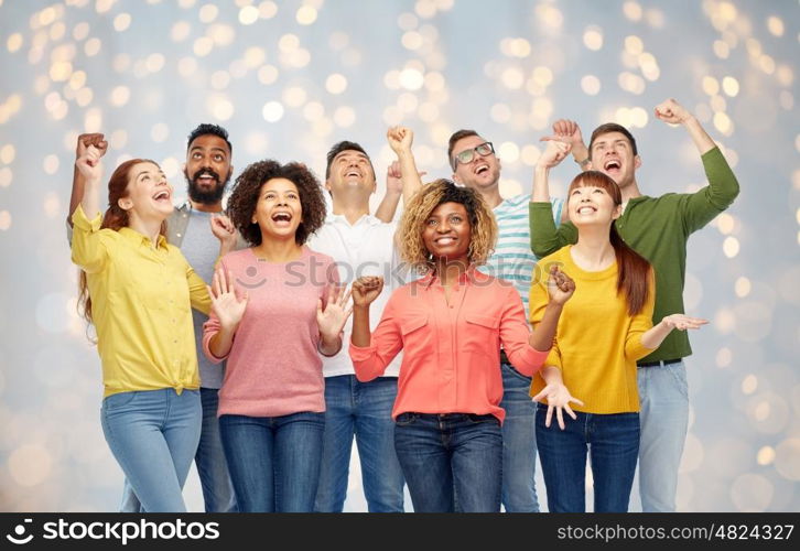 diversity, race, ethnicity, success and people concept - international group of happy smiling men and women celebrating victory over holidays lights background