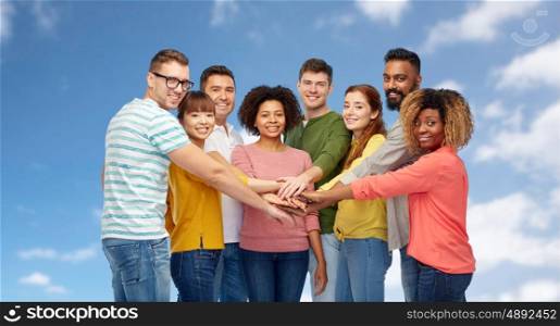 diversity, teamwork, race, ethnicity and people concept - international group of happy smiling men and women holding hands together over blue sky and clouds background