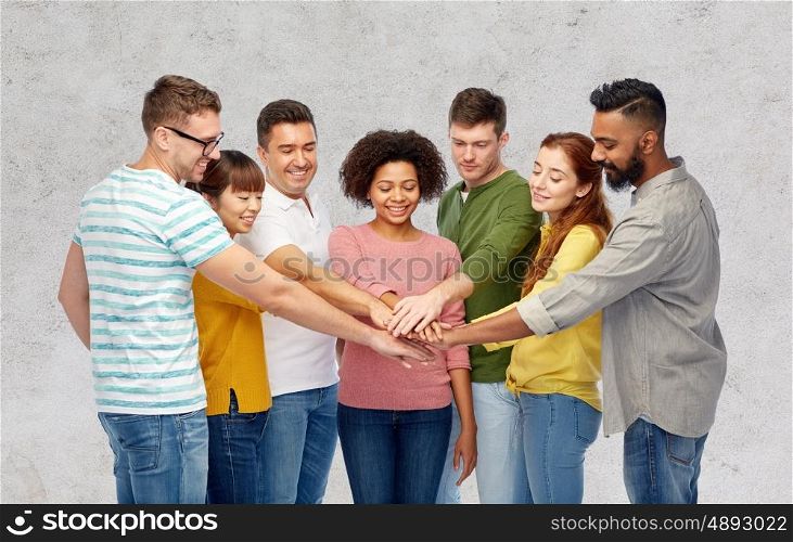 diversity, teamwork, race, ethnicity and people concept - international group of happy smiling men and women holding hands together over gray concrete background