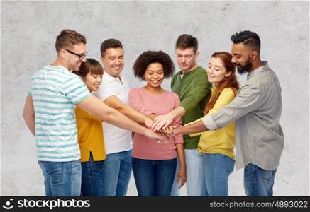 diversity, teamwork, race, ethnicity and people concept - international group of happy smiling men and women holding hands together over gray concrete background