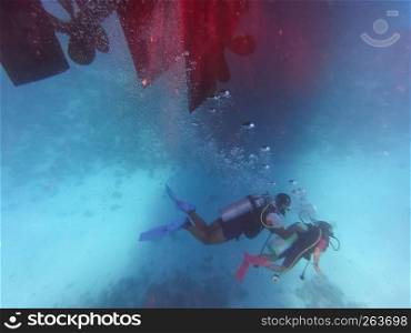 Diving people underwater in sea with corals and fish around, scuba diver open waters beginner course with professional instructor and young kid first time exploring challenging swimming under water
