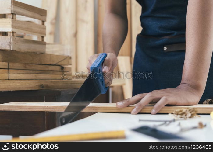 DIY woodworking and furniture making and craftsmanship and handwork concept. Carpenter working on woodworking machines in carpentry shop. Young man working as carpenter and taking wood stock.